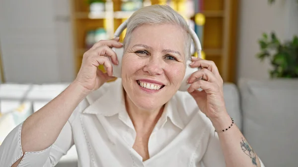 Middle age grey-haired woman listening to music sitting on sofa at home