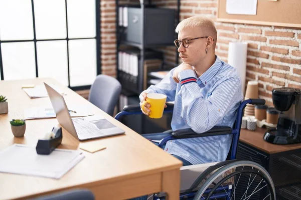 Young caucasian man business worker drinking coffee sitting on wheelchair at office