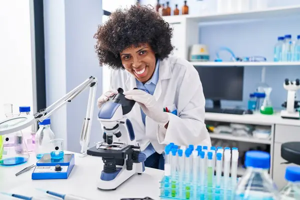African american woman scientist smiling confident using microscope at laboratory