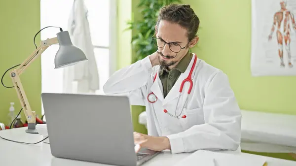 若いヒスパニックの男性医師は 診療所で子宮頸部の痛みに苦しむノートパソコンを使用しています — ストック写真