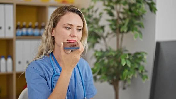 若いブロンド女性医師使用コンピュータ送信音声メッセージによるスマートフォンによってクリニック — ストック写真