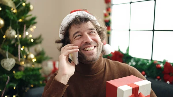 Νεαρός Ισπανόφωνος Μιλάει Στο Smartphone Κάθεται Στον Καναπέ Κρατώντας Χριστουγεννιάτικο — Φωτογραφία Αρχείου