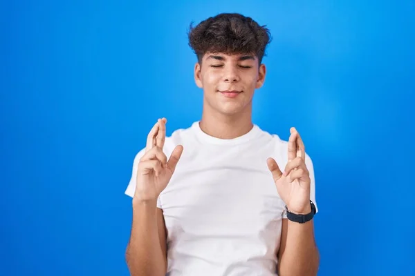 Латиноамериканский Подросток Стоящий Синем Фоне Жестом Скрестив Пальцы Улыбаясь Надеждой — стоковое фото