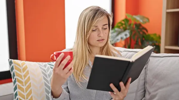 Mladá Blondýna Žena Čtení Knihy Pití Kávy Sedí Pohovce Doma — Stock fotografie