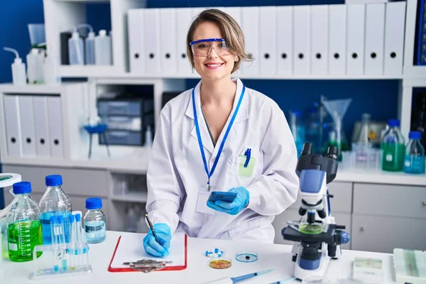 Young woman scientist writing report using smartphone at laboratory