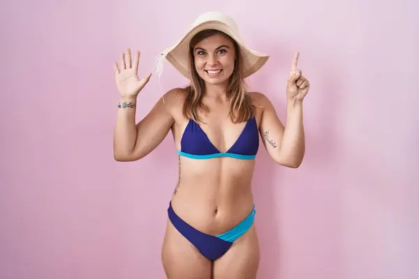 Young hispanic woman wearing bikini over pink background showing and pointing up with fingers number six while smiling confident and happy.