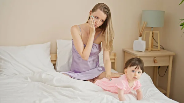 Mother and daughter sitting on bed with sad expression at bedroom