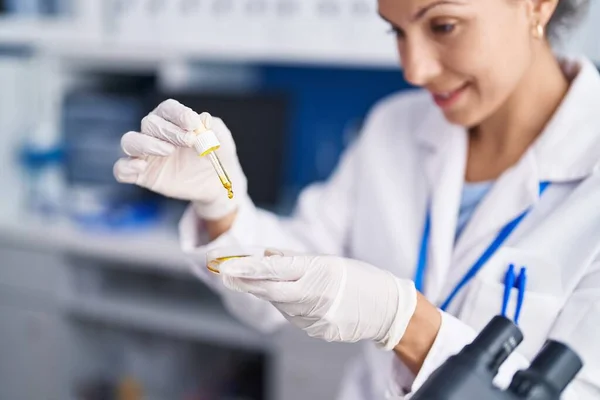 Young woman scientist pouring liquid on sample at laboratory