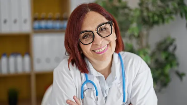 Middle age woman doctor smiling confident sitting on table at the clinic