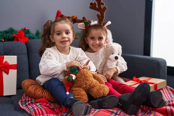 自宅でクリスマスの装飾でソファーに座っているテディベアを抱えている2人の子供 — ストック写真