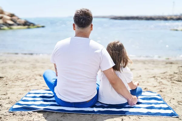 Father and daughter hugging each other sitting on sand at beach