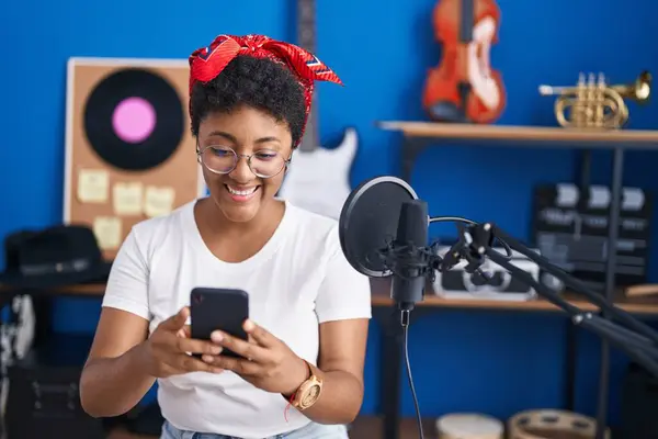 アフリカ系アメリカ人女性音楽家が音楽スタジオでスマートフォンを使って自信を持って笑う — ストック写真