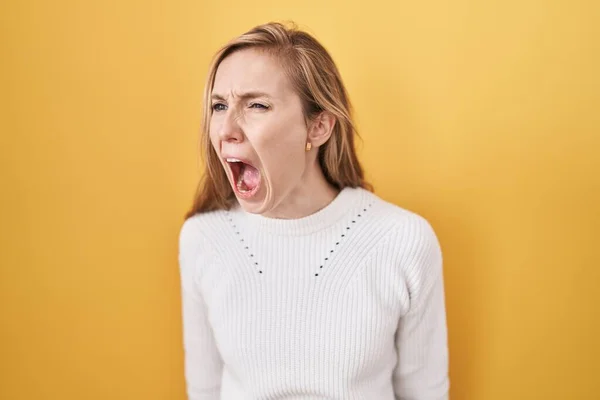 黄色い背景に白いセーターを着た若い白人女性は怒り狂い 怒って叫び 怒って叫びました 怒りと攻撃的な概念 — ストック写真