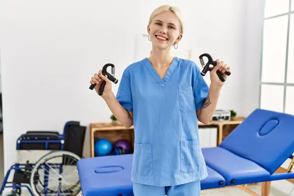 若い金髪女性理学療法士 リハビリクリニックでプレスハンドツールを保持する自信を持って微笑む — ストック写真