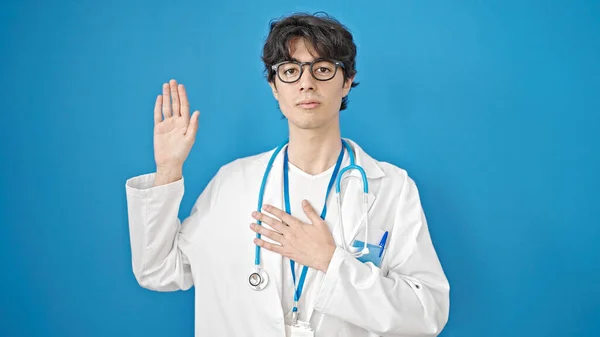 年轻的惊慌失措的男医生 手托着胸膛在孤零零的蓝色背景下宣誓 — 图库照片