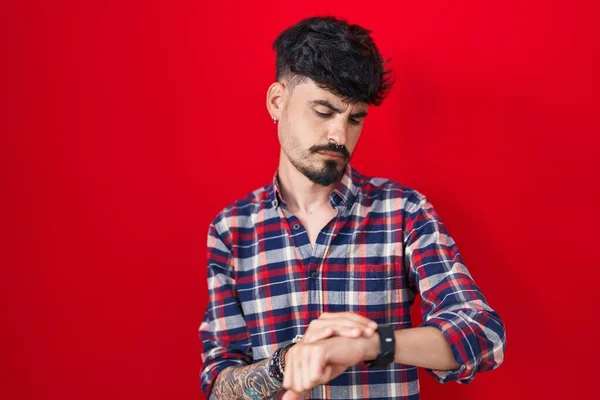 Kırmızı Arka Planda Duran Sakallı Genç Spanyol Adam Kol Saatinde — Stok fotoğraf