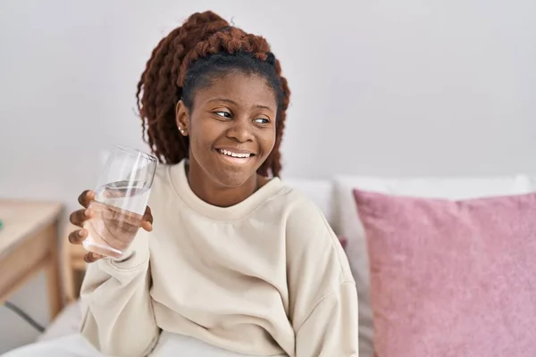 アフリカ系アメリカ人女性飲料水のガラスベッドルームでベッドに座って — ストック写真