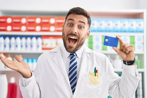 Bonito Homem Hispânico Trabalhando Farmácia Farmácia Segurando Cartão Crédito Celebrando — Fotografia de Stock