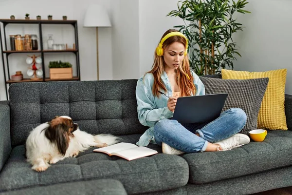 Young caucasian woman sitting on sofa with dog studying at home
