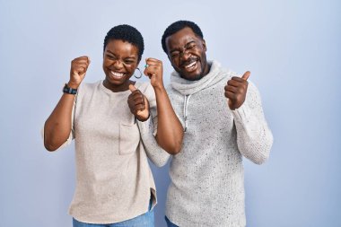 Mavi arka planda birlikte duran genç Afro-Amerikan çift kollarını kaldırmış ve gözleri kapalı zaferi kutluyorlar. Kazanan konsept. 