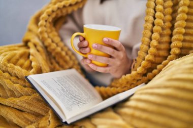 Genç İspanyol kadın kitap okuyor ve evde kahve içiyor.