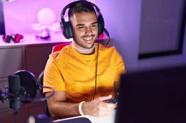 Young hispanic man streamer playing video game using joystick at gaming room