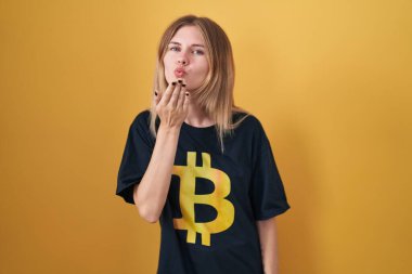 Bitcoin tişörtü giyen sarışın beyaz kadın kameraya bakıp havada bir öpücük savuruyor ve güzel ve seksi oluyor. aşk ifadesi. 