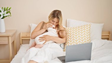 Anne kız bebek emziriyor dizüstü bilgisayarda film seyrediyor yatak odasında öpüşüyorlar.