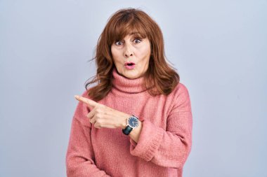 Orta yaşlı, ispanyol bir kadın izole edilmiş arka planda durup parmağını yana uzatarak şaşırmış ve ağzı açık bir şekilde hayret içinde kalmış.. 