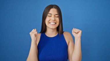 Genç, güzel İspanyol kadın gülümsüyor. Kendine güveni tam. Mavi arka planda bir jest yapıyor.