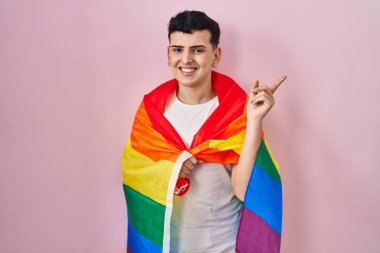 İkili olmayan kişi elinde gökkuşağı lgbtq bayrağı tutarken mutlu bir şekilde gülümsüyor. 