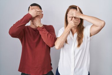 Anne ve oğlu izole edilmiş arka planda yan yana duruyorlar gözleri ve ağzı ellerle kaplıyorlar, şaşırmış ve şoktalar. duygu gizleme 