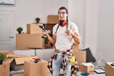 Yeni evinde elinde tornavidayla gülümseyen, mutlu ve pozitif gülümseyen uzun saçlı İspanyol bir adam. 