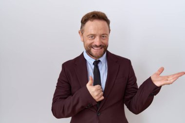Orta yaşlı, sakallı ve kravatlı bir iş adamı avuç içini gösteriyor ve baş parmaklarıyla iyi bir hareket yapıyor, mutlu ve neşeli gülümsüyor. 
