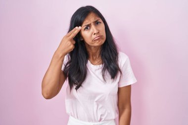 Young hispanic woman standing over pink background shooting and killing oneself pointing hand and fingers to head like gun, suicide gesture. 