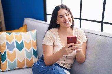 Evdeki kanepede oturan akıllı telefon kullanan genç, güzel İspanyol kadın.