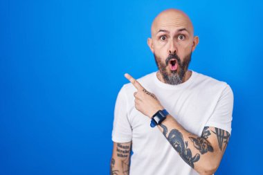 Mavi arka planda dikilen İspanyol dövmeli adam parmağını yana çevirerek şaşırdı, ağzı açık hayret içinde kaldı.. 