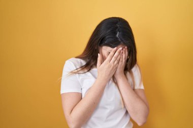 Sarı arka planda duran genç esmer kadın. Ağlarken suratını ellerle kapatan üzgün bir ifade. depresyon kavramı. 