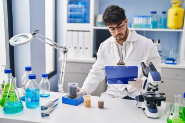 Young hispanic man scientist weighing sample reading document at laboratory