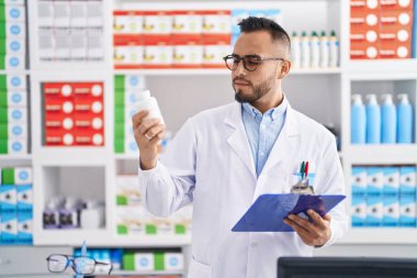 Eczanede ilaç şişesi tutan genç bir İspanyol eczacı eczanede evrak okuyor.