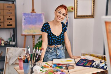 Beyaz kadın sanatçı, sanat stüdyosunda kendine güvenerek gülümsüyor.