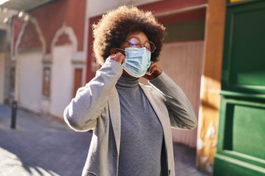 Sokakta tıbbi maske takıp gülümseyen Afrikalı Amerikalı kadın yönetici.