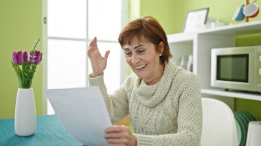 Olgun İspanyol kadın yemek odasındaki masada oturmuş evrak okuyor.