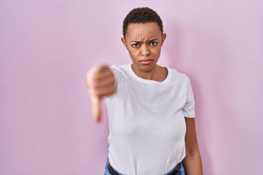 Güzel Afro-Amerikalı kadın pembe arka planda duruyor mutsuz ve kızgın görünüyor reddediliyor ve olumsuz bir hareket yapıyor. kötü ifade. 