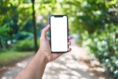 Akıllı telefonu tutan adam parkta beyaz ekranı gösteriyor.