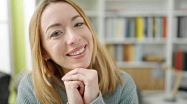 Kütüphanede masada oturmuş gülümseyen genç sarışın kız öğrenci.