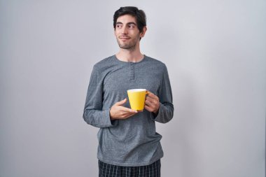 Genç İspanyol adam pijama giyiyor bir fincan kahve içiyor gülümsüyor ve yan tarafa bakıyor ve düşünüyor.. 