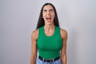 Young woman standing over isolated background angry and mad screaming frustrated and furious, shouting with anger. rage and aggressive concept. 