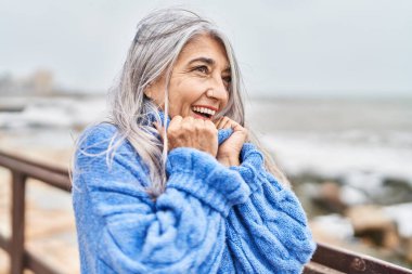 Middle age grey-haired woman smiling confident looking to the side at seaside