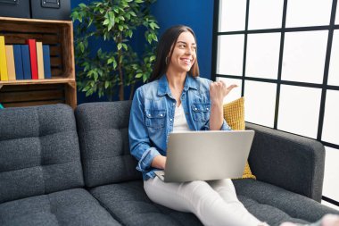 Evde dizüstü bilgisayar kullanan İspanyol bir kadın parmak ucunda ağzı açık bir şekilde gülümsüyor. 